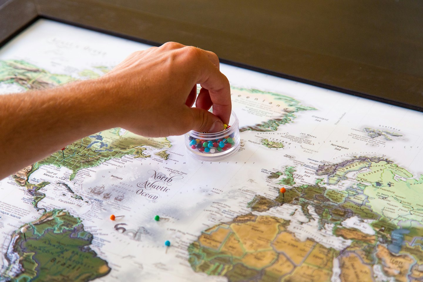 Hand selects a push pin from a container for a world map.