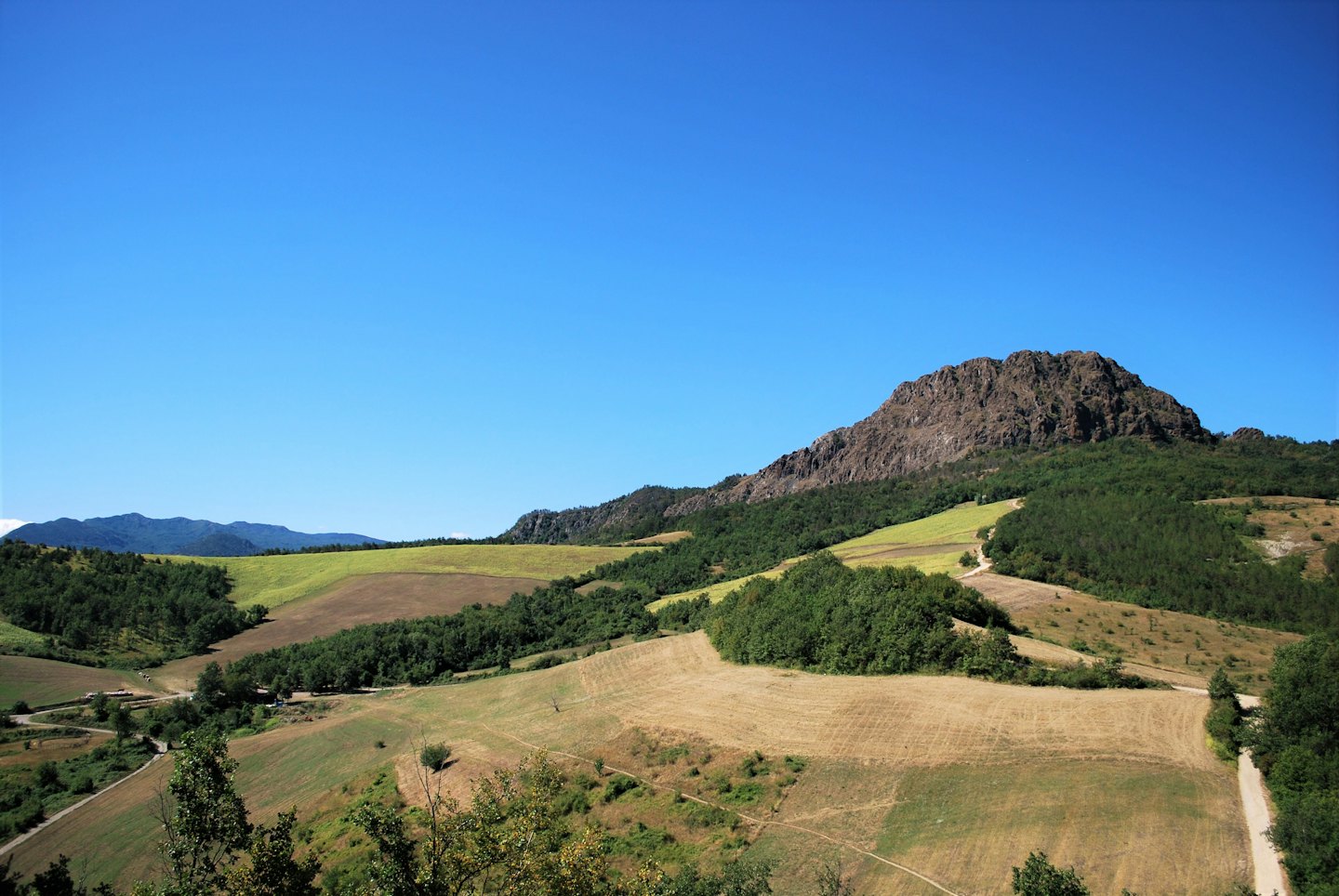 Rolling green hills and dry fields meet a rocky mountain peak.