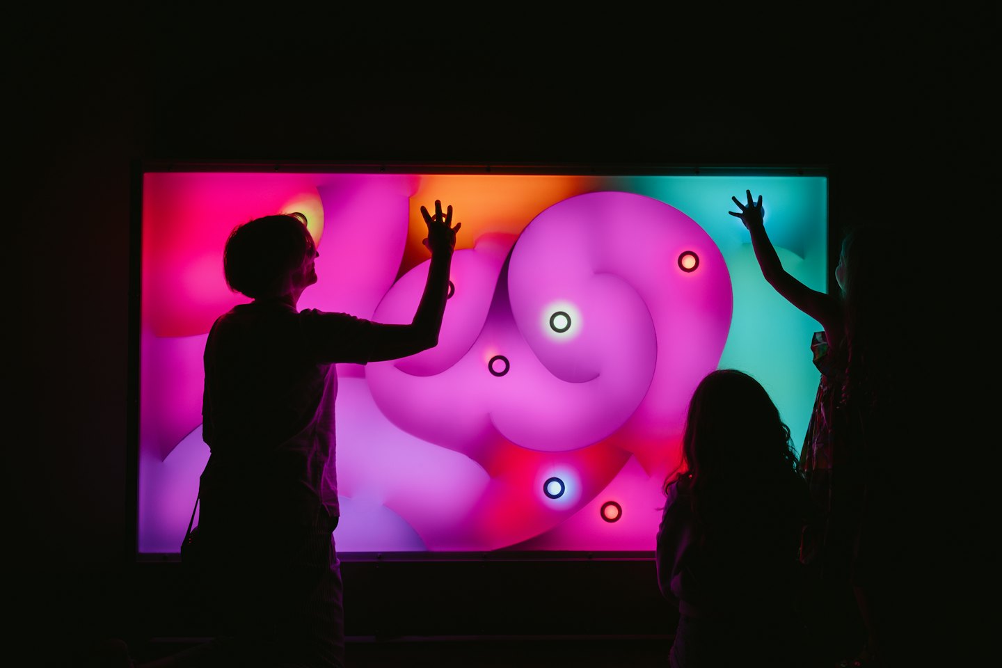 An adult and two children touching an interactive display screen.