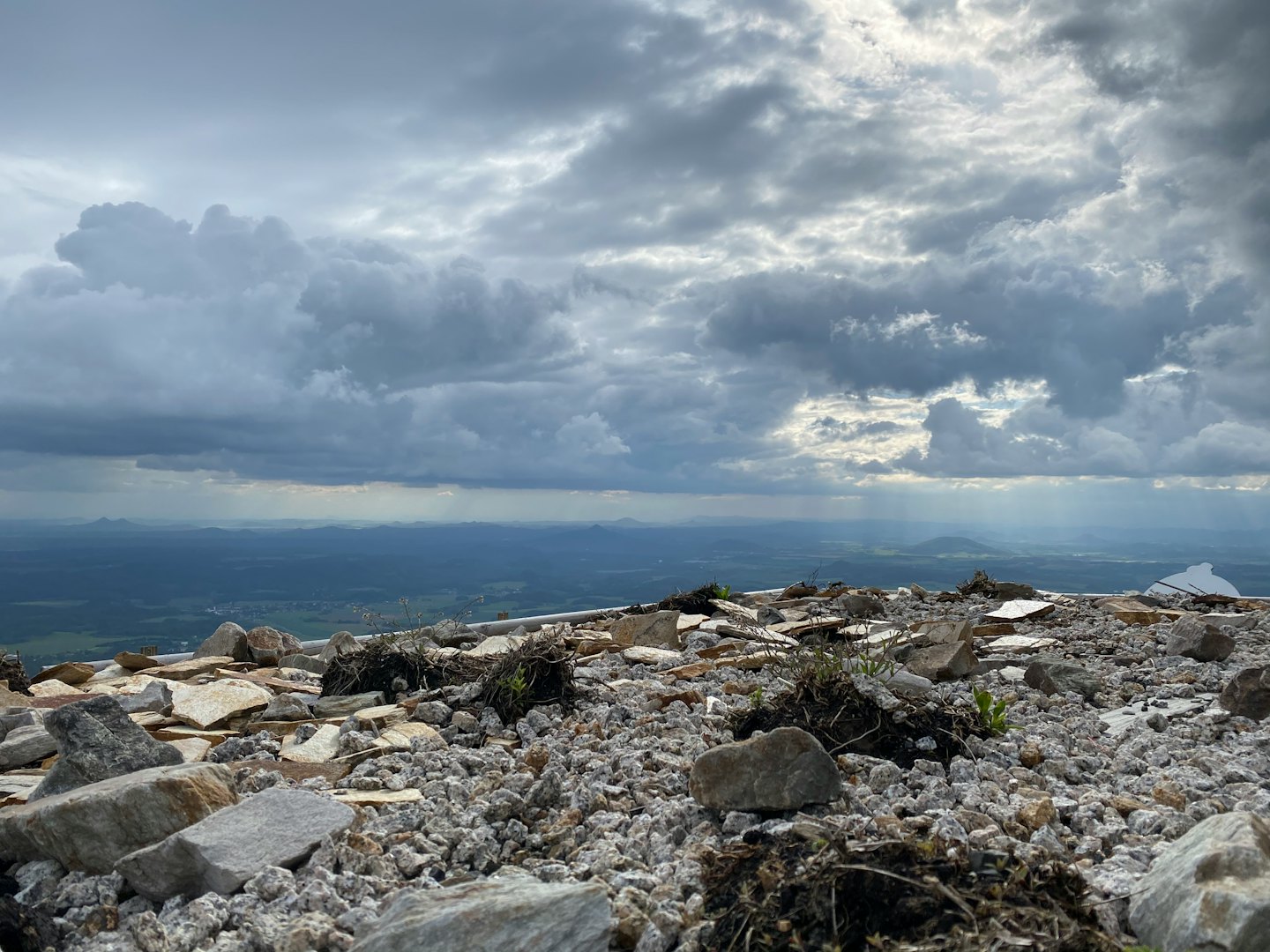 Rocky mountain peak overlooking a vast landscape under cloudy skies.